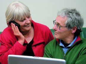 Äldre par framför en bärbar dator som tittar på varandra medan kvinnan talar i telefon